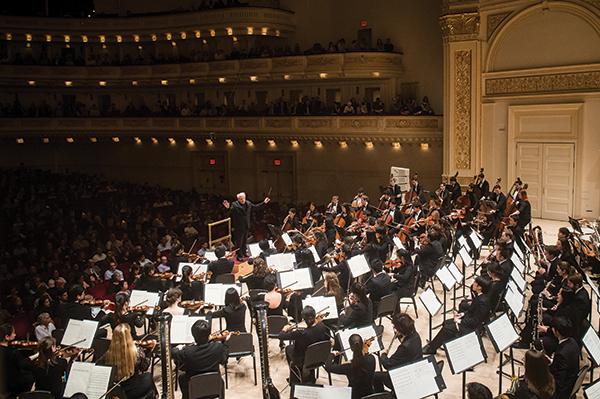 orchestra on stage at carnegie hall conducted by man